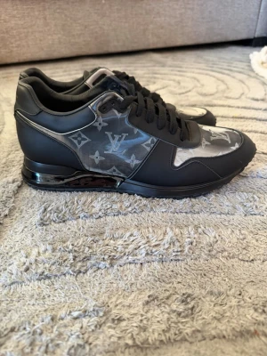 Louis Vuitton Runaway Sneakers  - Snygga svarta sneakers från Louis Vuitton med klassiskt monogrammönster i grått och silver. Skorna har svarta snören, mattsvarta detaljer och en stilren siluett i lågt utförande. Materialmix av läder och textil ger en exklusiv känsla.
