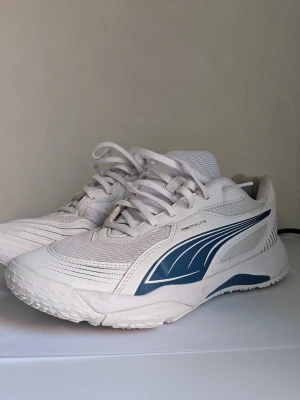 Vita Puma sneakers med blå detaljer 40 - Snygga vita sneakers från Puma med blå sidodetalj och meshpaneler för extra andningsförmåga. Skorna har klassisk låg profil, vita snören och en robust sula som passar perfekt till streetwear eller sportiga outfits.  Mycket gott skick .
