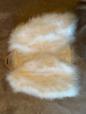 Vit fluffig väst/bolero av strutsfjädrar - Supermjuk vit väst med silkeslen insida. Västen har en klassisk öppen modell. Perfekt för att lyfta din outfit med en trendig touch. 40 cm lång, 40 cm axel till axel. Äldre vintage i fint skick. Cremevit.