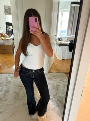 Mörkblå bootcut jeans ( gina tricot young) - Säljer ett par mörkblå bootcut jeans med vita kontrastsömmar och stora fickor bak. Jeansen har låg midja och klassisk femficksdesign. Perfekta för dig som gillar en retro och trendig look.