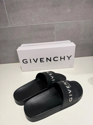 Svarta Givenchy slides med logga - Givenchy tofflor i storlek 43, kommer med orginallåda och dustbags. Mindre synliga tecken på användning. Perfekta inför sommaren!