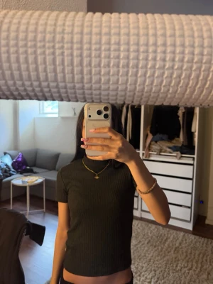 Svart ribbad kortärmad topp - En svart ribbad topp med korta ärmar och rund halsringning. Toppen har en slim passform och är tillverkad i ett stretchigt material som sitter snyggt på kroppen. Perfekt att styla med jeans eller kjol för en trendig look.
