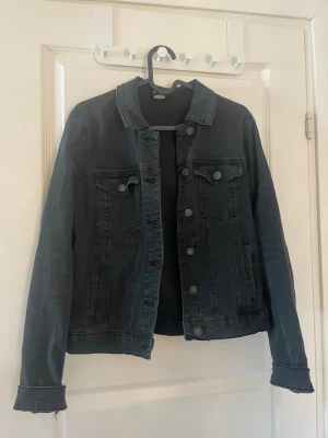 Jeansjacka - Snygg svart jeansjacka med raka linjer och klassisk krage. Jackan har två bröstfickor med lock och knappar. Storleken är M men skulle säga att den passar en person från xs-m. Den är använd fåtalet gånger och har inga tecken på slitage