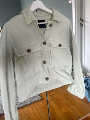 Ljusgrön jeansjacka från Zara - Trendig ljusgrön jeansjacka från Zara med stora bröstfickor och snygga knappar framtill. Jackan har klassisk krage, långa ärmar och en avslappnad passform. Perfekt att slänga över en t-shirt för en cool look.
