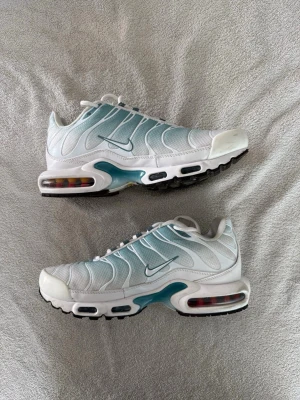 Nike tns - Nike Air Max Plus sneakers i vitt och ljusblått med ikoniska vågformade detaljer och synlig Air Max-dämpning i sulan. Skorna har mesh-överdel, vita snören och svarta yttersulor. Perfekta för dig som gillar sportig och modern stil.