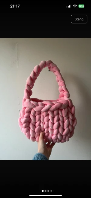 Chunky rosa stickad handväska - Superfin handväska i chunky stickad design, gjord av tjockt, mjukt garn i en härlig ljusrosa färg. Väskan har en rundad form och ett rejält handtag, perfekt för dig som vill sticka ut med en unik accessoar. Ingen synlig logga eller märke.