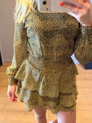 Leopardmönstrad volangklänning - Kort klänning med leopardmönster och volangdetaljer. Klänningen har långärmade, lätt transparenta ärmar och smock i midjan för en snygg passform. Endast använd ett fåtal gånger 💗
