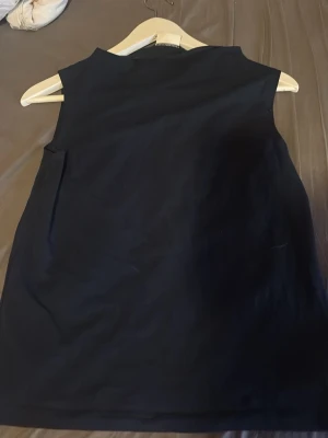 Svart ärmlös topp från Kappahl - En stilren svart ärmlös topp från Kappahl. Toppen har en rak passform och hög halsringning, perfekt att matcha med jeans eller kjol. Tillverkad i mjukt material som känns skönt mot huden.
