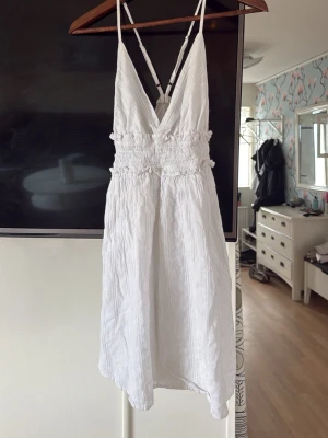 Vit sommarklänning med smock - Luftig vit klänning med smala axelband och v-ringning fram. Smockad midja ger en snygg passform och klänningen har en kort längd. Perfekt för varma dagar och enkel att styla med accessoarer. Den är från shein, så de kan va dålig kvalitet. Säljer den ändå då jag inte tycker man borde slänga kläder, aldrig använd.