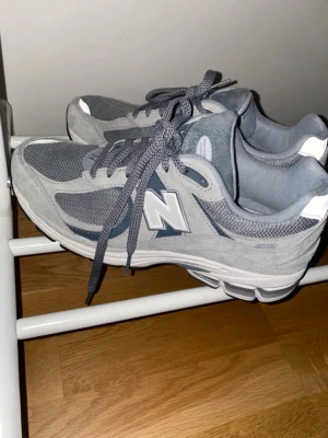 Grå New Balance 2002r sneakers - Säljer ett par klassiska New Balance 2002R sneakers i grått. Skorna har mesh och mocka på ovandelen, ikoniskt N-märke på sidan och bekväm dämpad sula. Perfekt för dig som gillar stilrena och sportiga sneakers med retrovibe. Endast använt 2 gånger 