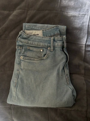 Ljusblå regular fit jeans - Säljer ett par ljusblå jeans i regular fit med klassisk femficksdesign och raka ben. Jeansen har bälteshällor och är tillverkade i mjukt denimtyg. Perfekta för en avslappnad och stilren look.