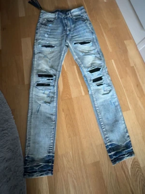 Amiri Ljusblå slitna jeans med hål - Säljer ett par ljusblå amiri jeans med kraftiga slitningar och stora hål på både lår och knän. Jeansen har skinny fit och klassisk femficksmodell. Perfekta för dig som gillar en edgy och trendig stil. Storlek är 30/32. 