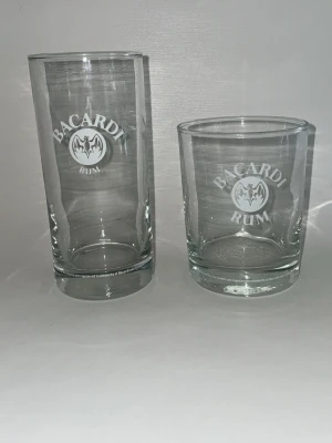 Bacardi glas  - 60kr glas  Bacardi glas i klart glas, ett högt och ett lågt. Båda har Bacardi-loggan och texten 'Bacardi Rum' tryckt i vitt på framsidan. Perfekta för drinkar eller samling. Snygg och stilren design.