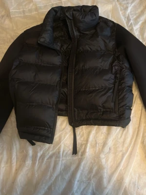 Svart pufferjacka från Zara - Snygg svart pufferjacka från Zara med hög krage och dragkedja framtill. Jackan har vadderade partier, släta svarta ärmar och en praktisk ficka med dragkedja på sidan. Perfekt för kalla vinterdagar och riktigt trendig look.