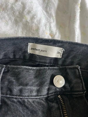 Svarta raka jeans från Perfect Jeans - Säljer ett par svarta raka jeans från Perfect Jeans i storlek 36. Jeansen har klassisk femficksmodell, hög midja och dragkedja med knapp. Materialet är kraftigt denim som ger en snygg och tidlös look.
