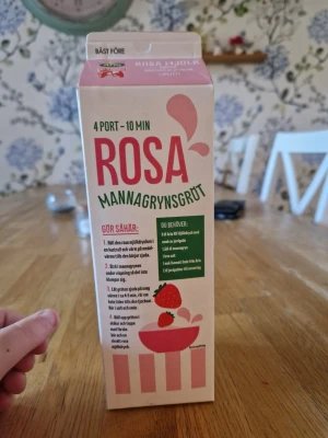 Rosa mannagrynsgröt med jordgubbssmak - En förpackning rosa mannagrynsgröt med smak av jordgubb. Innehåller instruktioner för tillagning och är perfekt för dig som vill ha något annorlunda till frukost eller mellanmål. Kartongen är vit och rosa med illustration av en skål gröt och jordgubbar.