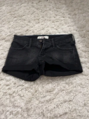 Svarta denimshorts med uppvik - Snygga svarta low waist denimshorts med uppvikta benslut och klassisk femficksdesign. Shortsen har knapp och dragkedja framtill samt bälteshällor. Perfekta till sommaren för en avslappnad och cool stil. säljwr pga för små