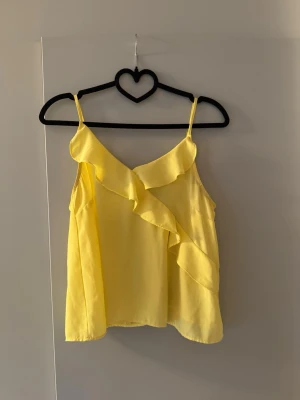 Gul volangtop från Gina Tricot - Snygg gul linnetopp från Gina Tricot med volangdetaljer framtill. Tunt och lätt material med smala axelband. 