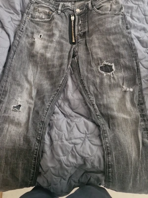Grå slitna jeans från Dan Caten - Säljer ett par grå jeans från Dan Caten med slitningar och hål för en riktigt edgy look. Jeansen har dragkedja fram, fem fickor och en cool tvättad finish. Perfekta för dig som gillar streetstyle och vill sticka ut.
