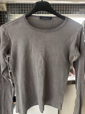 Grå ribbad långärmad brandy Melville - Säljer en grå ribbad långärmad topp från Brandy Melville. Toppen har ett diskret randigt mönster och är i en mjuk, stretchig bomullsblandning. Perfekt basplagg med rund halsringning och slim passform.