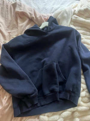 Mörkblå hoodie från Gina Tricot - Mörkblå hoodie från Gina Tricot med klassisk huva och stor magficka. Tillverkad i mjukt bomullsmaterial och har ribbade muddar vid ärmslut och nederkant. Perfekt för en chill och avslappnad stil.