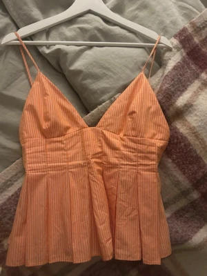  Ny trendig Randig orange linnetopp med smala axelband - Säljer en söt orange linnetopp med vita smala ränder och tunna axelband. Toppen har v-ringad hals och lätt utsvängd passform nedtill. Perfekt för varma dagar och enkel att styla med jeans eller kjol.