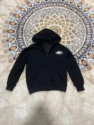 Corteiz zip M - Svart Corteiz hoodie med dragkedja framtill och huva,storlek M men passar mer som S. På bröstet och ryggen finns det en corteiz logga. Hoodien har ribbade muddar vid ärmar och nederkant.