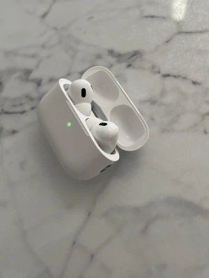 Hörlurar  - Säljer ett par vita hörlurar med trådlöst laddningsetui. Hörlurarna har en stilren och kompakt design i blank plast och passar perfekt för musik, samtal och träning. Smidig magnetisk förvaring i etuiet och LED-indikator på framsidan.