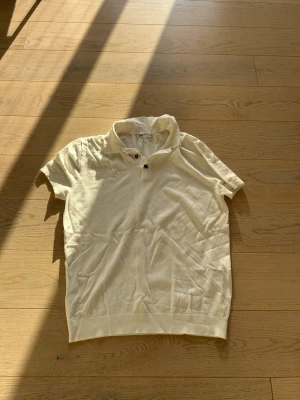 Vit kortärmad polotopp från Zara - Klassisk vit polotopp från Zara med korta ärmar och två knappar vid kragen. Tillverkad i mjukt bomullsmaterial och har en avslappnad passform. Perfekt till jeans eller kjol för en enkel och stilren look. Är storlek M fast passar mycket bättre som S