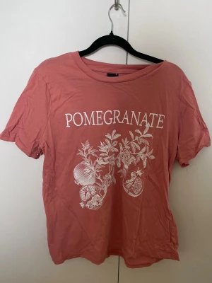 Rosa t-shirt med print från Gina Tricot - Trendig rosa t-shirt från Gina Tricot med vitt tryck av granatäpple och texten 'POMEGRANATE' på bröstet. 
