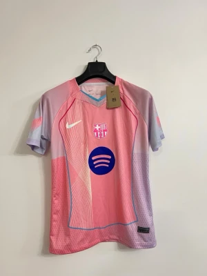 FC Barcelona tröja  Nike    S - Snygg rosa och lila FC Barcelona matchtröja från Nike med klubbmärke och Nike-logga på bröstet samt Spotify-logga i blått. Tillverkad i lätt och ventilerande funktionsmaterial, perfekt för fotboll eller träning. Unik design med grafiska detaljer och korta ärmar.