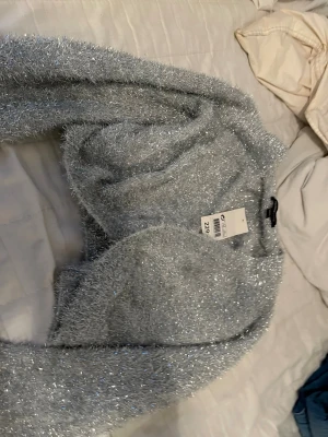 Glittrig silverstickad tröja - Supermjuk och glittrig stickad tröja i silver från mywear young. Tröjan har lång ärm och fluffig textur med metallictrådar som ger en riktigt festlig look. Perfekt för dig som vill sticka ut med en cool och trendig stil.