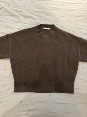 Brun stickad tröja från Zara - Mysig brun stickad tröja från Zara med rund halsringning och bred ribbstickad kant nedtill och vid ärmslut. Tröjan har en avslappnad passform och är perfekt för lager på lager under kyliga dagar.