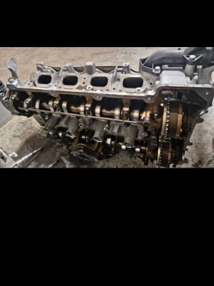 Bil motorblock i metall - Säljer ett motorblock till bil, tillverkat i metall med synliga kamaxlar och kedjedrivning. Motorblocket har flera öppningar för insug och är i en grå och bronsfärgad ton. Perfekt för dig som gillar att meka med bilar eller behöver reservdelar.