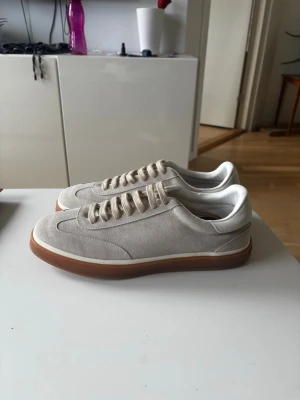 Loro Piana Tennis walk - Stilrena beige sneakers i mocka med vita detaljer och klassisk brun gummisula. Lågt skaft och matchande beige snörning ger en clean look. Perfekta för dig som gillar minimalistisk och tidlös stil.