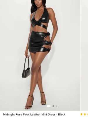 Svart cut-out miniklänning från Fashionnova - Snygg svart miniklänning i fejkskinn med cut-out detaljer och knytningar i sidan. Halterneck-modell med djup v-ringning och tight passform. Perfekt för dig som vill sticka ut och gillar trendiga statement-plagg.