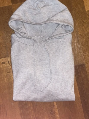 Grå kachmir hoodie  med snörning - En stilren grå hoodie med huva och snörning. Tröjan har långa ärmar, ribbade muddar och är tillverkad i mjuk bomullsmix. Perfekt för chill dagar eller när du vill ha en enkel och clean look.