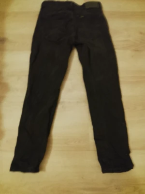 Svarta Lee jeans med smal passform - Säljer ett par svarta jeans från Lee med smal passform och klassisk femficksdesign. Jeansen har en diskret Lee-logga på linningen och är tillverkade i ett slitstarkt denimtyg. Perfekta för dig som gillar en enkel och stilren look.