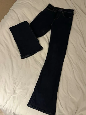 Mörkblå bootcut jeans - Säljer ett par mörkblå bootcut jeans i klassisk denim. Jeansen har normal midja och vida ben som ger en snygg retrovibe. Perfekta att styla med sneakers eller boots för en avslappnad look. Från only. Storlek xs/32