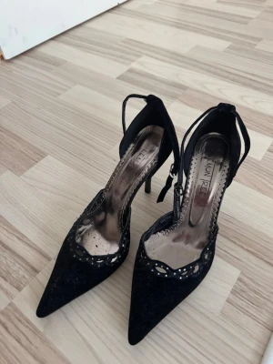 Svarta spetsiga pumps - Snygga svarta pumps från Lemon Ree med spetsig tå och smal klack. Materialet ser ut att vara mockaimitation med glansiga detaljer.