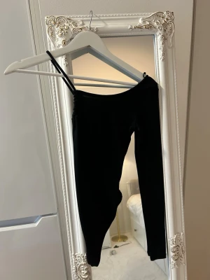 Svarta body med en arm - De har en enkel design utan synliga detaljer och är tillverkade i ett stretchigt material som sitter tajt mot kroppen. 