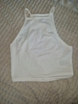 croppad linnetopp från HM Divided - Enkel och stilren vit croppad topp, smala axelband och hög halsringning, perfekt till sommaren. Tillverkad i mjuk bomull för en bekväm känsla.