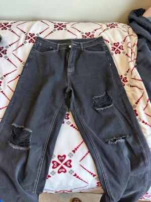 Svarta ripped jeans med vida ben - Säljer ett par svarta jeans med vida ben och slitna detaljer på båda benen. Jeansen har hög midja, fem fickor och synliga vita sömmar. Perfekta för en avslappnad och trendig look. Materialet är klassisk denim i bomull.