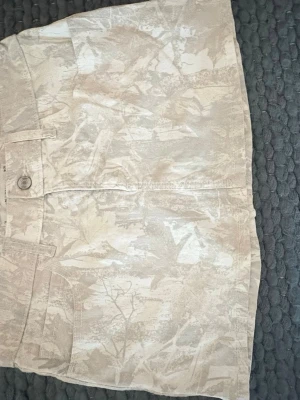 Beige kjol från Hollsiter  - Säljer en beige kortkjol med camouflageinspirerat mönster. Köpte i somras och bara använd en gång. Hör av dig vid frågor! 