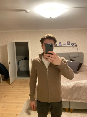 Brun ribbad ziptröja med hög krage - Säljer en brun ribbad ziptröja med hög krage och långa ärmar. Tröjan har en hel dragkedja framtill och är tillverkad i ett mjukt stickat material. Perfekt för lager på lager och enkel att matcha med olika outfits.