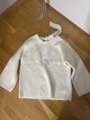 Vit stickad tröja med rosett - Säljer en söt vit stickad tröja med rund halsringning och en stor dekorativ rosett i bak och öppen rygg. Lämna gärna prisförslag!