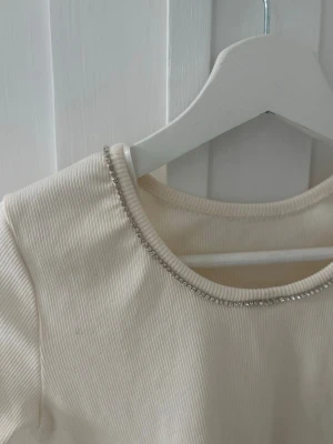 Vit ribbad topp med pärldetalj - Snygg långärmad topp i ribbat vitt tyg med silver pärlor vid halsen,har bara använt tröjan en gång🩷