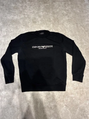 Svart sweatshirt Emporio Armani - Stilren svart sweatshirt från Emporio Armani med vit logga och text på bröstet. Tröjan är i fint skick och har du frågor tveka inte att ställa!                                   Pris kan diskuteras vid snabb affär!