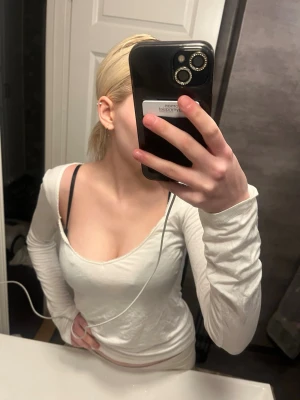 Vit långärmad topp med v-ringning - Säljer en enkel och stilren vit långärmad topp med djup v-ringning. Toppen har en slim passform och är perfekt att matcha med jeans eller kjol. Materialet känns mjukt och stretchigt, troligen bomull eller en bomullsblandning. Storlek M men sitter som S ungefär.