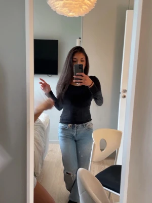 Zara Jeans - Säljer ett par ljusblå jeans med raka ben och slitningar på båda knäna. Jeansen har klassisk femficksmodell och knappgylf. Perfekta för en avslappnad och trendig look.